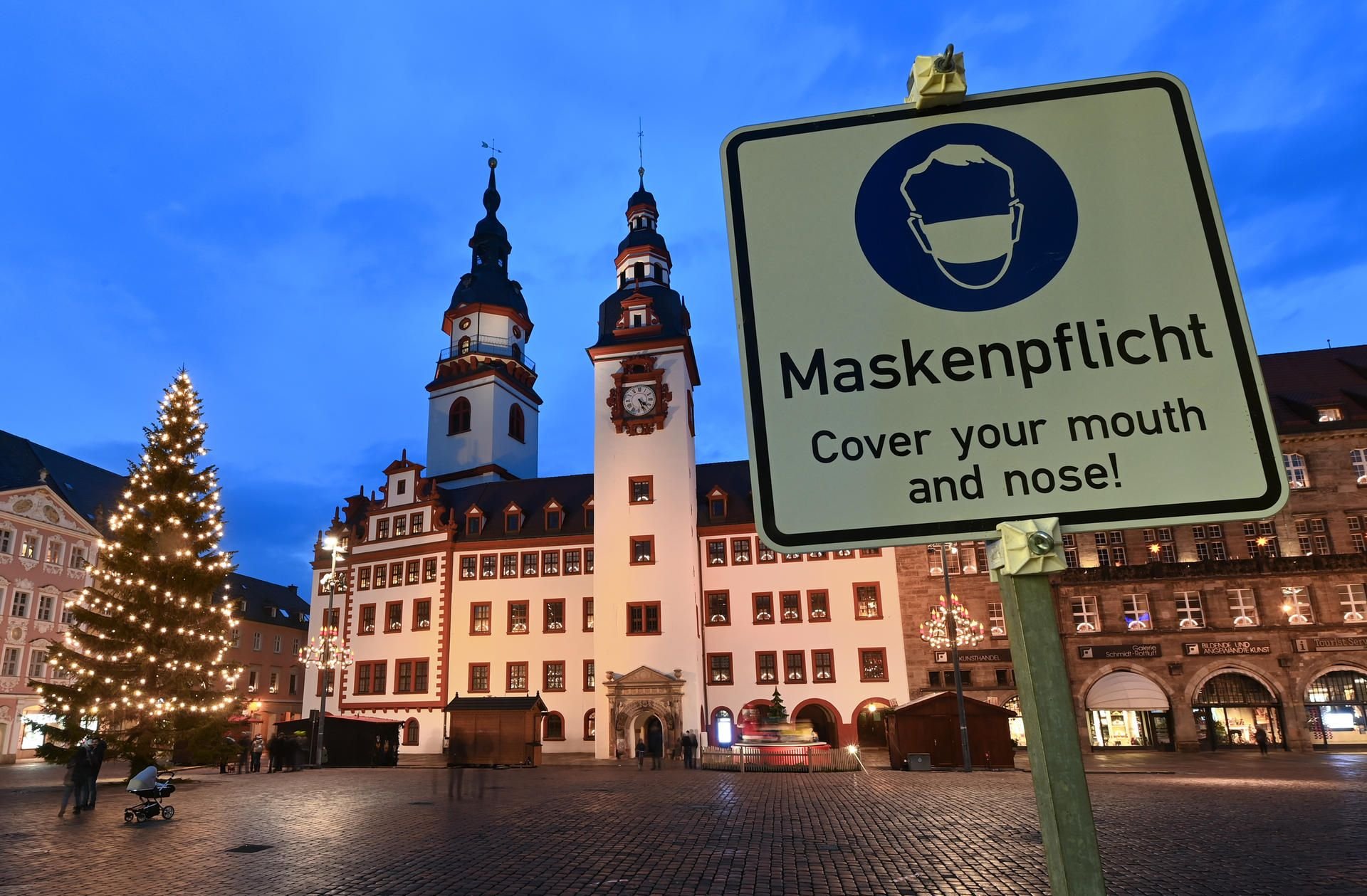 Chemnitz: Ein Schild mit der Aufschrift "Maskenpflicht" steht am weihnachtlich beleuchteten Markt vor dem Alten Rathaus.