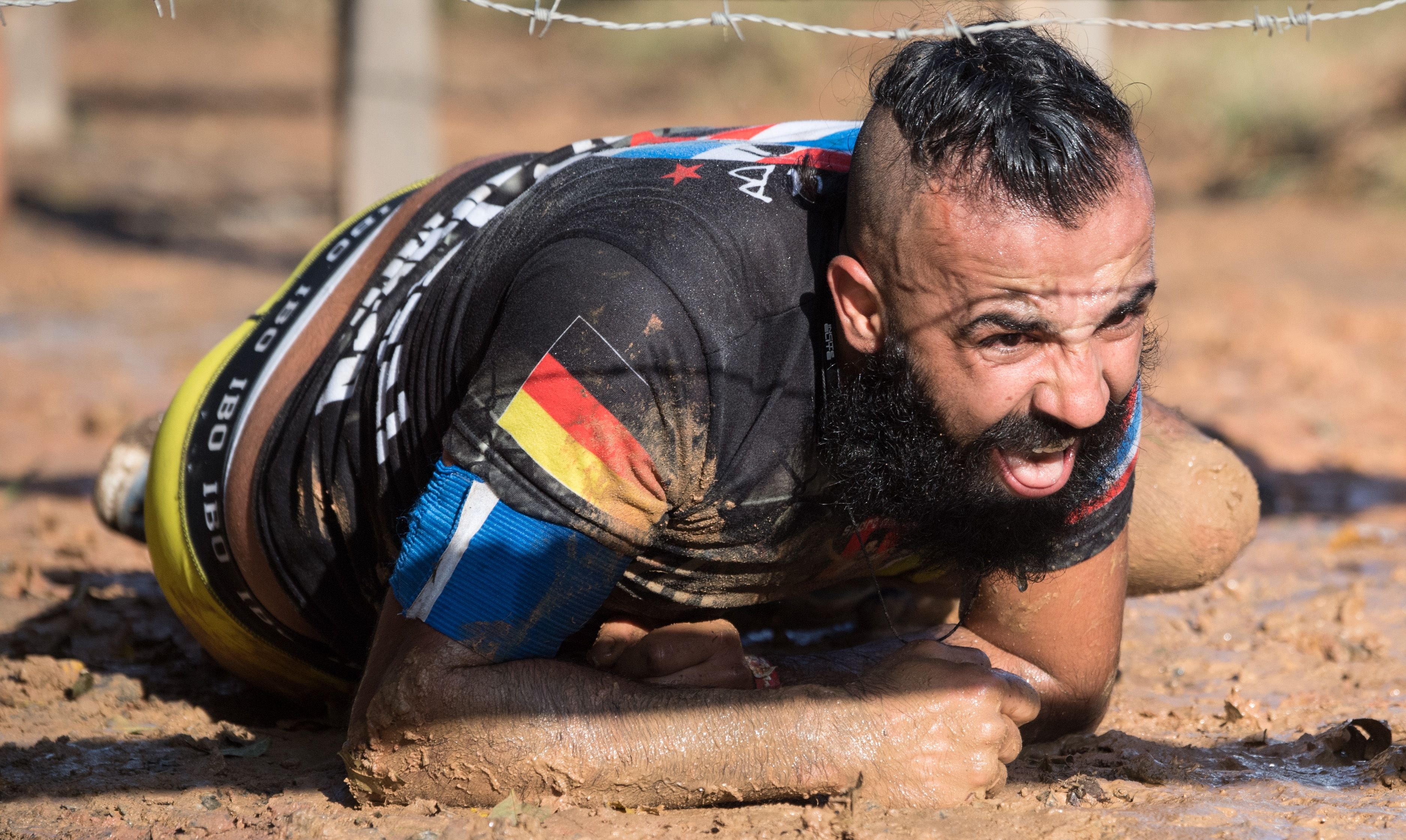 Unter einem Holzgestell mit Stacheldraht hindurch robbt ein Teilnehmer bei der Marathon-Variante des "Iron Viking" Wettbewerbs in Wächtersbach (Hessen) durch den Matsch.