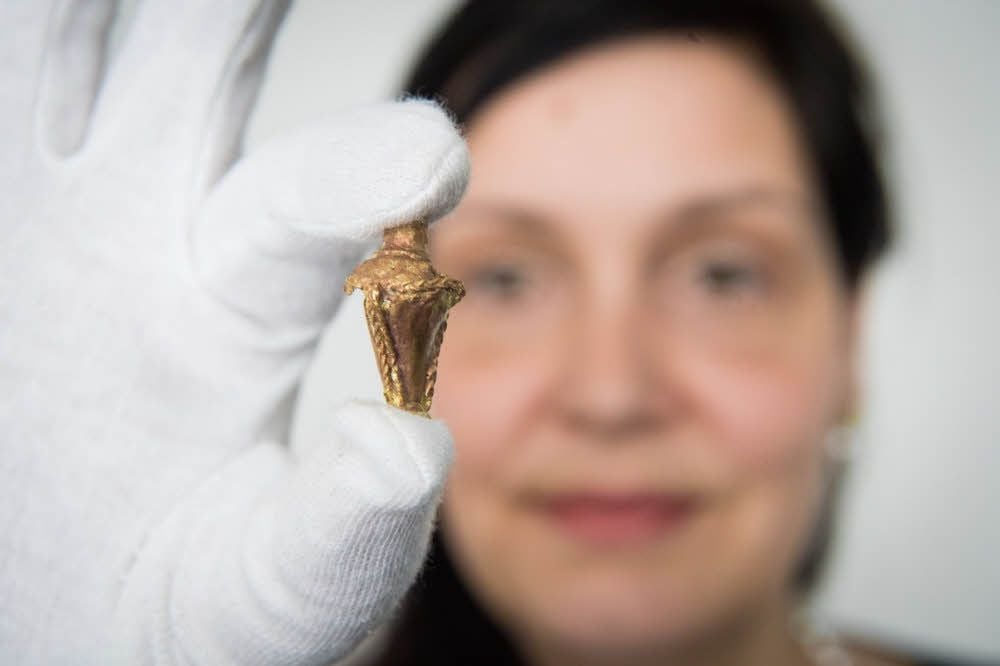 Mit Schutzhandschuh: Bettina Pfaff, Geschäftsführerin der Arche Nebra, hält einen sogenannten Goldberlock, einen Anhänger, aus dem dritten Jahrhundert in die Kamera.