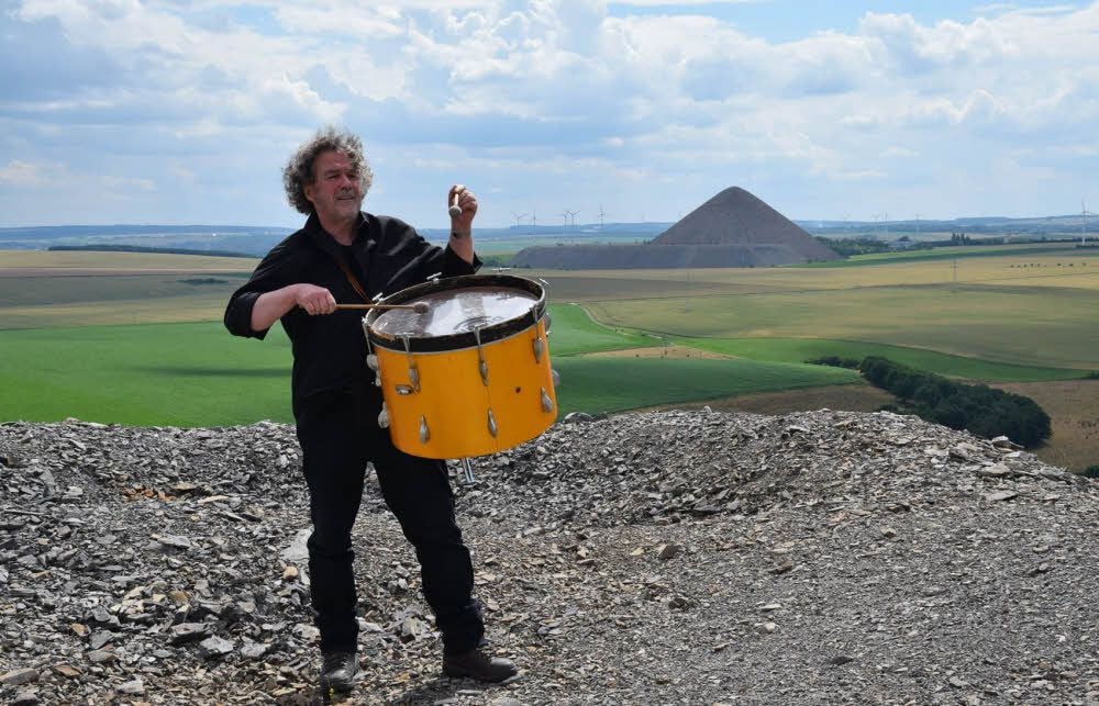 Liedermacher Hans-Jürgen Radam trommelt voller Inbrunst auf der Spitze der Brosowski-Halde, im Hintergrund der Thälmannschacht.