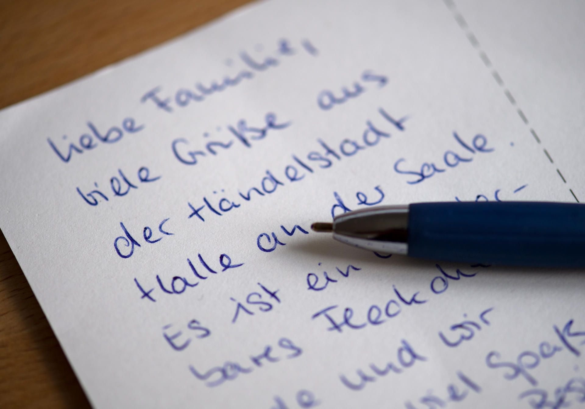 Eine Postkarte mit Grüßen aus Halle/Saale liegt auf einem Schreibtisch.