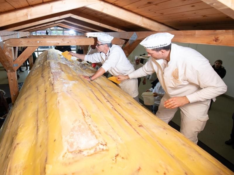 Bäcker der Schutzgemeinschaft Dresdner Stollen streichen Butter und Zucker auf den Riesenstollen. Foto: Sebastian Kahnert/dpa-Zentralbild/dpa