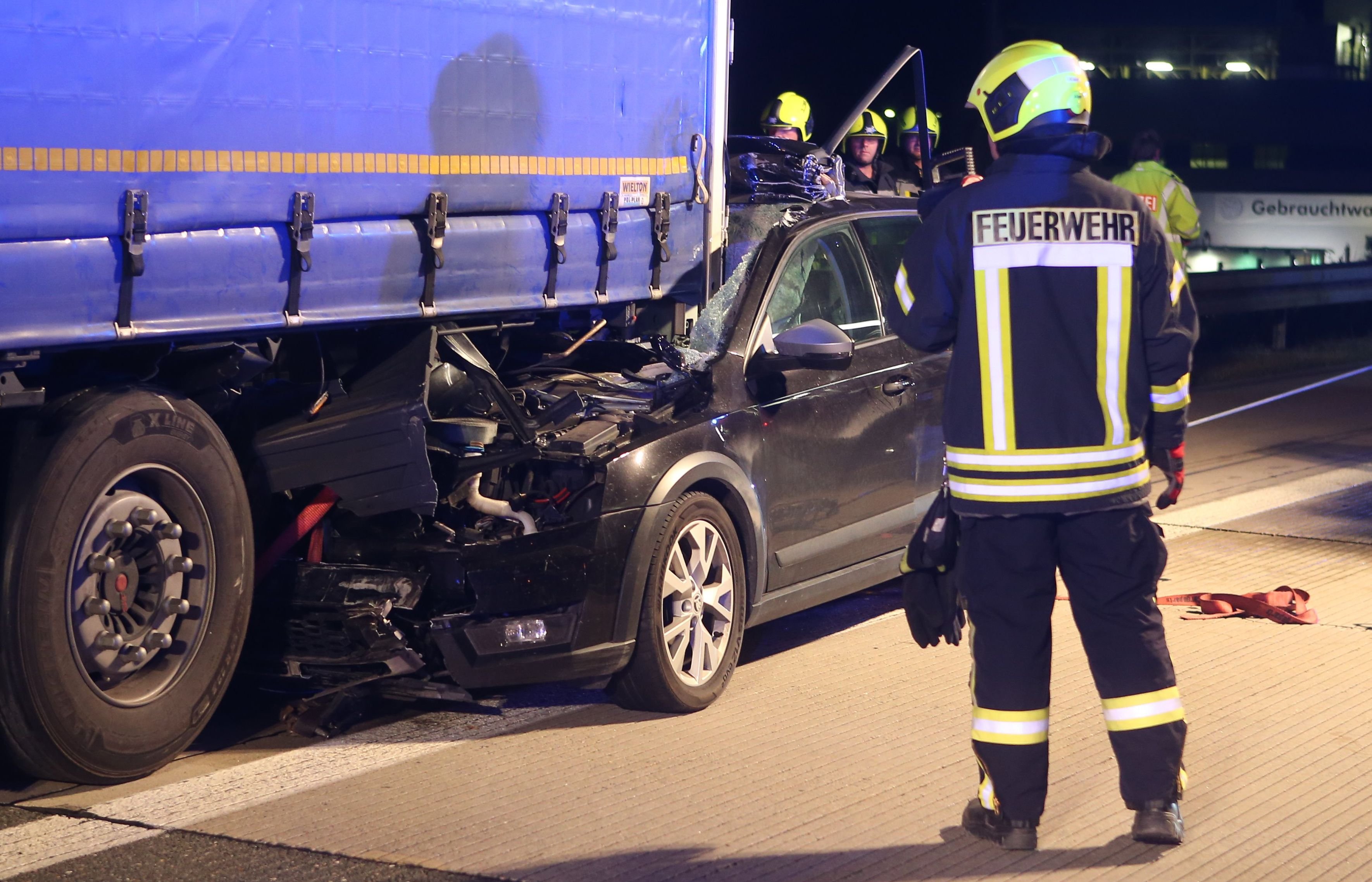 Ein Feuerwehrmann steht an einer Unfallstelle auf der Autobahn 4 bei Gera vor einem Auto, das unter einen Lastwagen eingeklemmt ist.