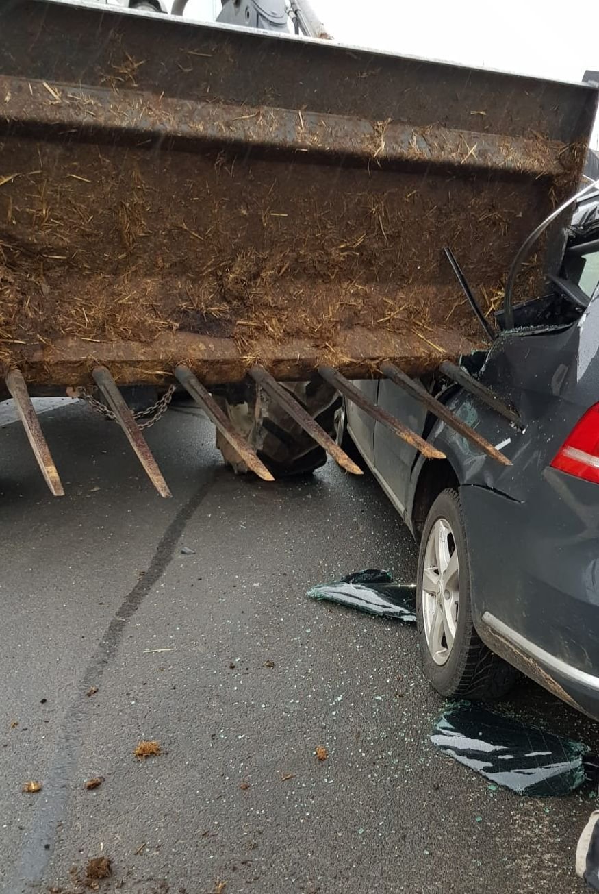 Die heruntergelassene Mistgabel eines Frontladers hängt nach einem Verkehrsunfall in der Seite eines Pkw.