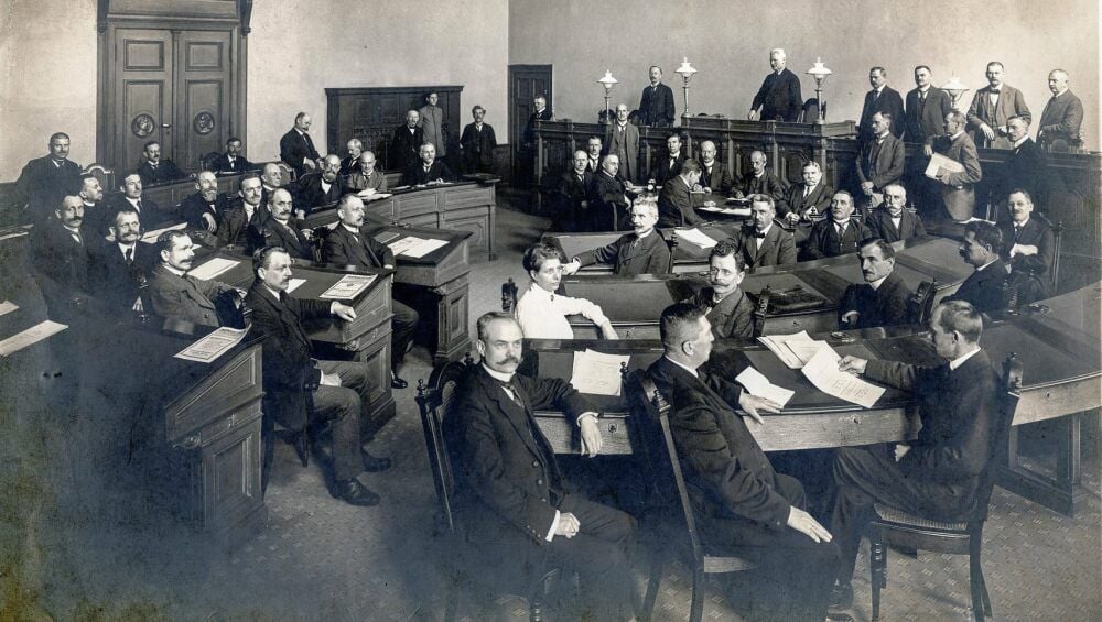 Eine Frau und 35 Herren gehörten 1919 zum Landtag des Freistaates Anhalt, der als erster im Deutschen Reich den Frauen Wahlrecht und Wählbarkeit zugestand. Marie Kettmann (2. Reihe, Mitte) wurde daher von Präsident Heinrich Peus (stehend am Pult) als erste Abgeordnete ausdrücklich begrüßt.
