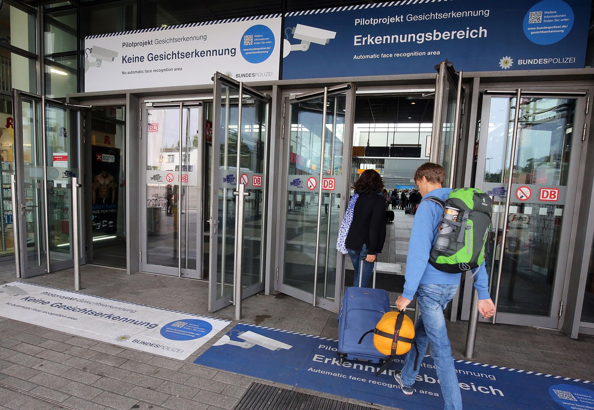 Passanten nutzen in Berlin am Bahnhof Südkreuz einen Eingang der mit „Pilotprojekt zur Gesichtserkennung" gekennzeichnet ist.