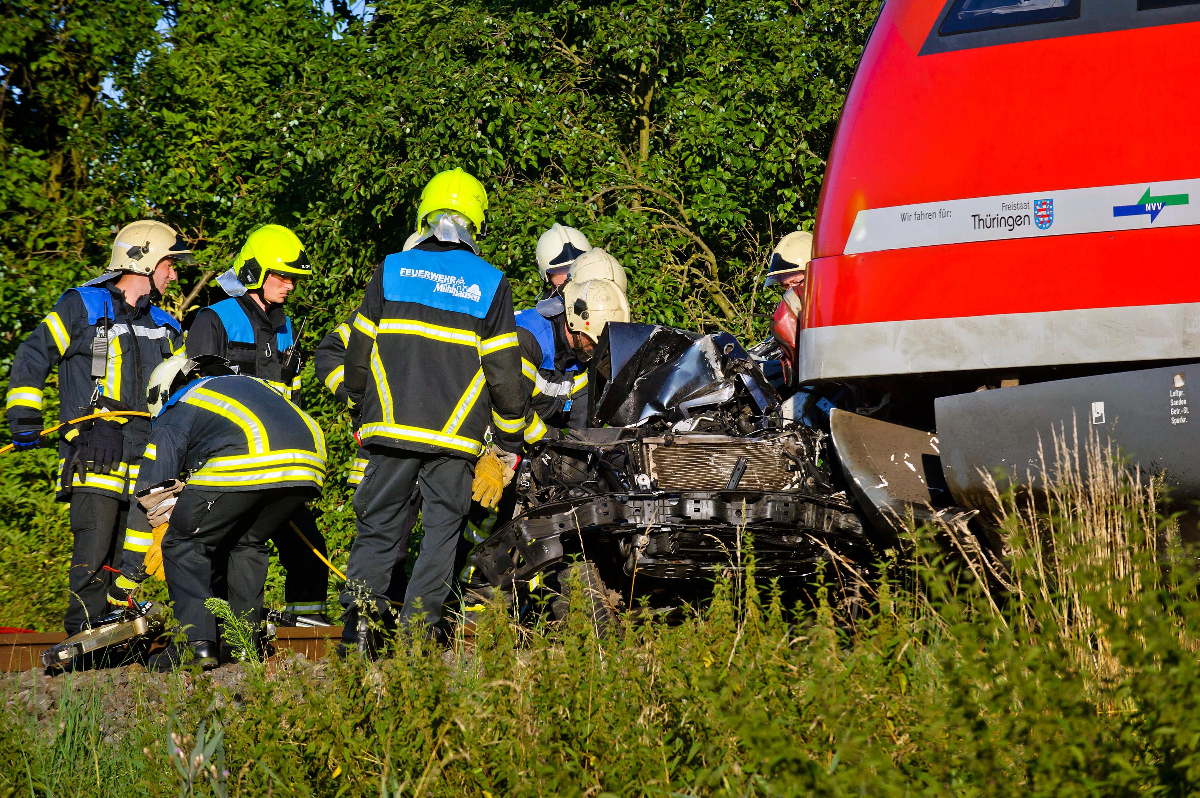 Feuerwehrleute stehen an einem Unfallort in Höngeda neben einem Auto, das bei einem Bahnübergang mit einem Regionalzug zusammengestoßen ist.