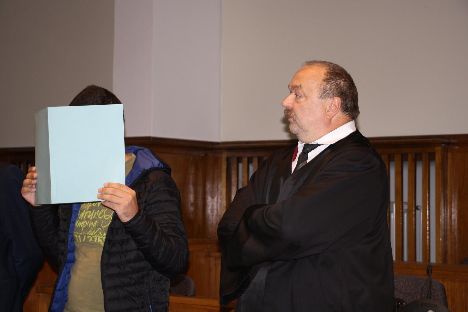 Der Angeklagte Mohammad A. (l) verdeckt in einem Saal des Landgerichts Saarbrücken sein Gesicht mit einem Aktendeckel, neben ihm steht sein Verteidiger Fred Valentin. Der 27-Jährige steht wegen Mordes an seinem Therapeuten vor Gericht.