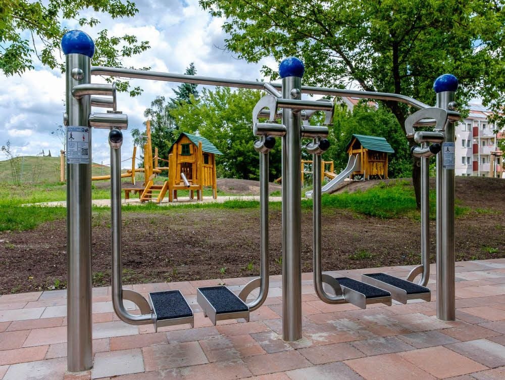 Der Beintrainer ist eines der drei Senioren-Sportgeräte, im Hintergrund ist der Kinderspielplatz zu sehen.