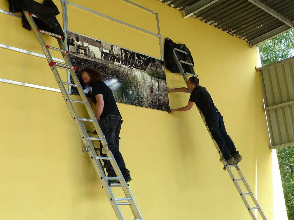 Mitarbeiter der Media GmbH aus Wolfen bringen auf der Freilichtbühne Tafeln an, auf der eine Collage der Stadt Bitterfeld-Wolfen zu sehen ist.