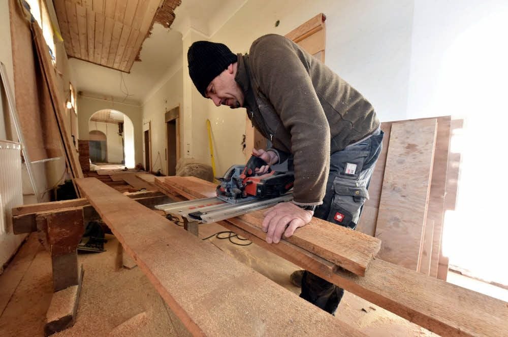 Danilo Pfeifer sägt im Flur des Herbergstraktes Holzbretter zu.