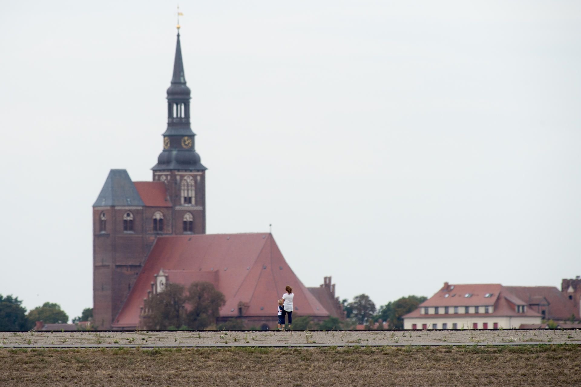 Fischbeck: Spaziergänger gehen über den fertiggestellten Deich. Im Hintergrund überragt der Dom in Tangermünde (l) und das Schloss den Erdwall.