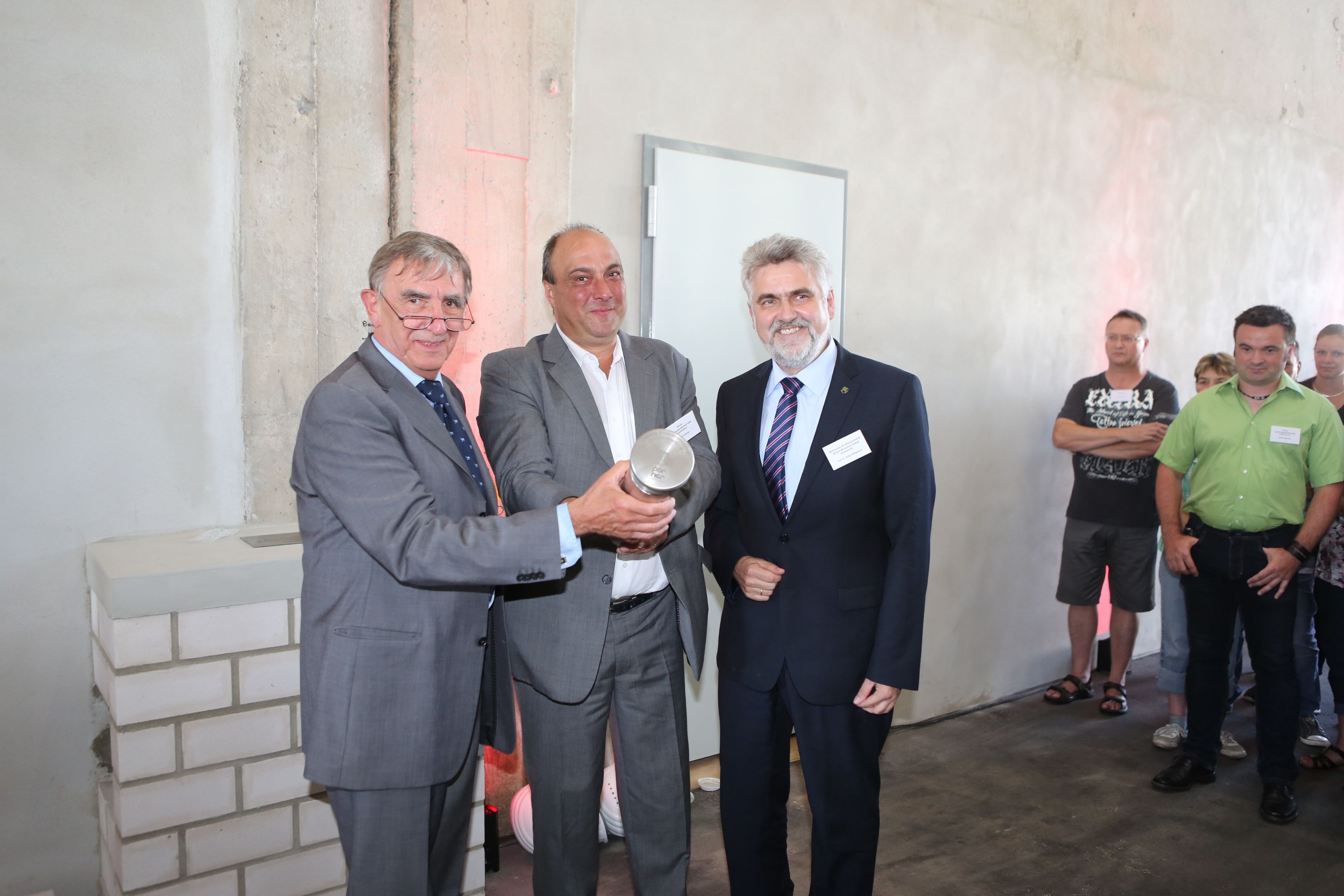 Geschäftsführer Bernd Schneider, Projektleiter Gerhard Bacher und Staatssekretär Armin Willingmann (v.l.) halten die Hülse mit vielen Dokumenten.
