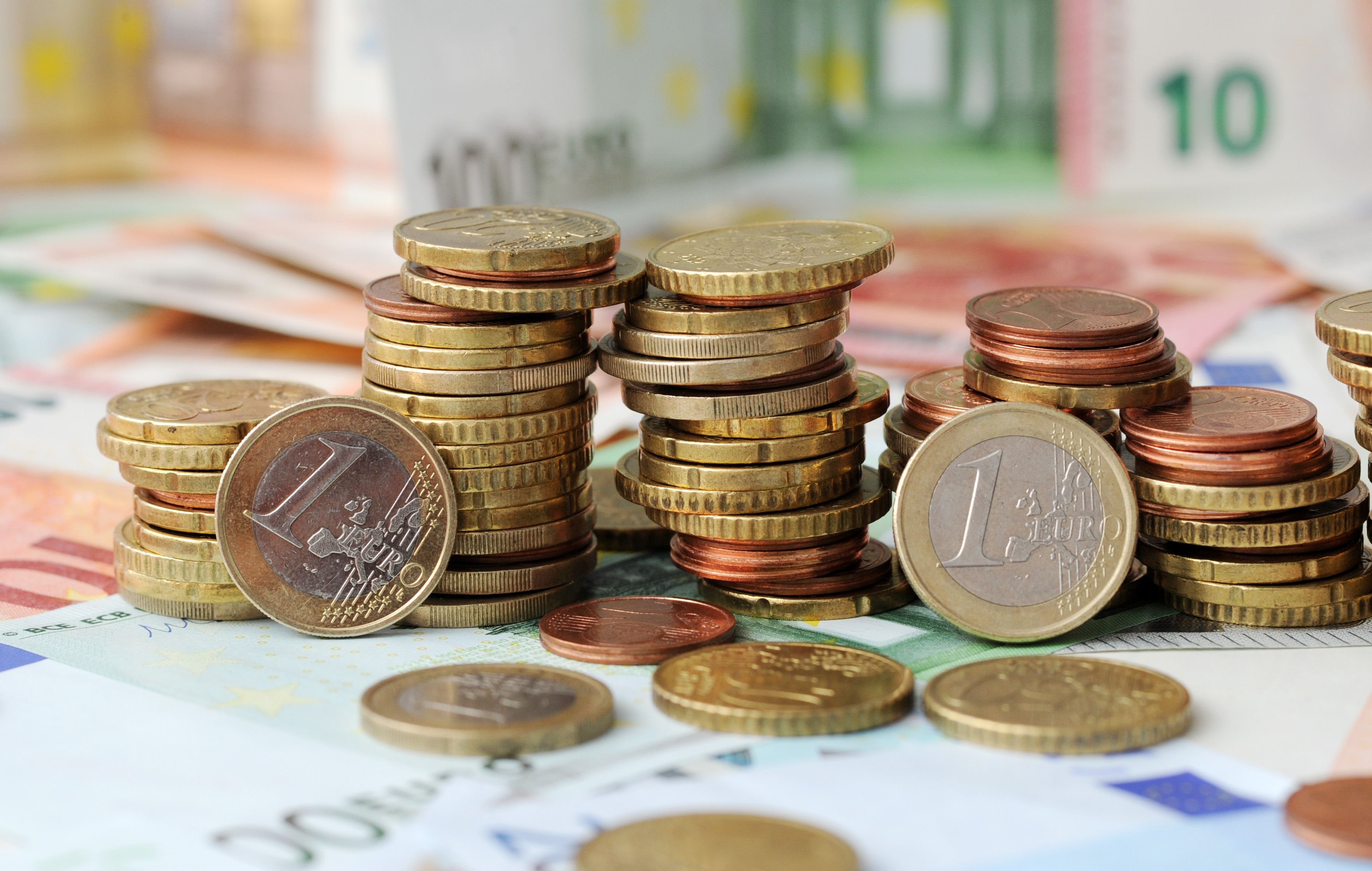 Gestapelte Geldmünzen liegen auf Geldscheinen.