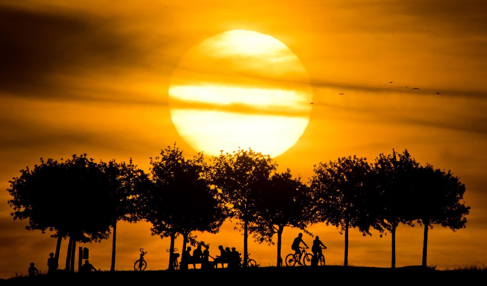 Die Silhouetten von Passanten zeichnen sich vor dem vom Sonnenuntergang verfärbten Abendhimmel ab. Nach dem ungewöhnlich heißen Sommer steht nun der Herbst vor der Tür.