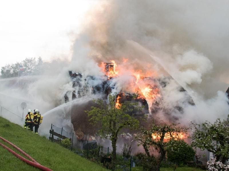 Feuerwehrleute löschen ein im Vollbrand stehendes Reetdachhaus. Foto: Daniel Bockwoldt/dpa