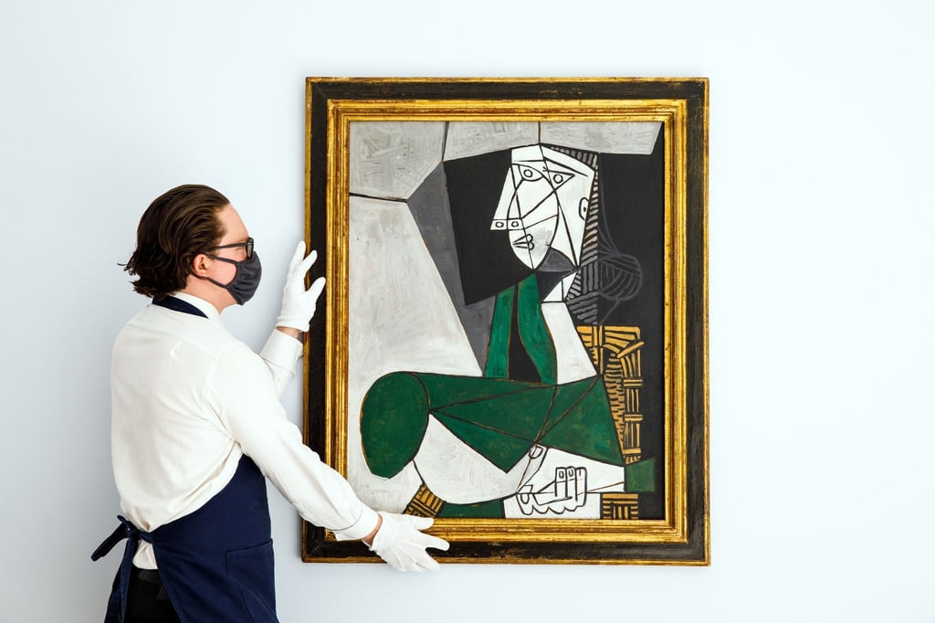 Ein Mitarbeiter von Sotheby's hängt das Gemälde „Femme assise en costume“ von Pablo Picasso (gemalt 1953) auf.