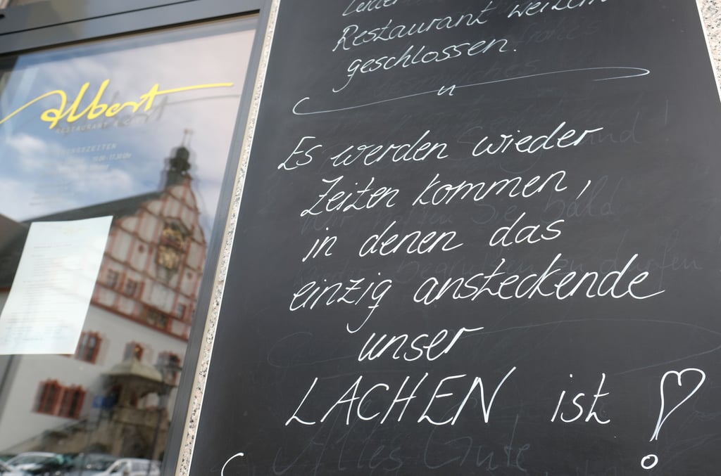 Auf einer Tafel an einem geschlossenen Restaurant in der Innenstadt steht "Es werden wieder Zeiten kommen, in denen das einzig ansteckende unser Lachen ist!".