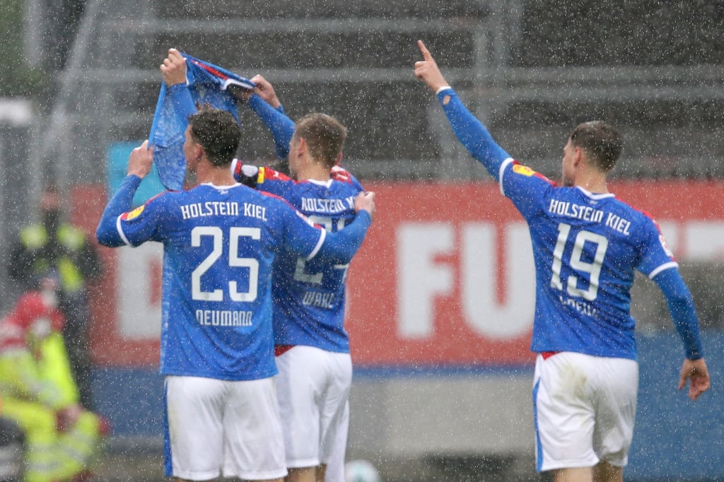 Die Kieler Spieler Phil Neumann (l-r), Hauke Wahl und Simon Lorenz halten nach dem Treffer zum 1:1 ein Trikot des verletzten Mannschaftskameraden Ahmet Arslan hoch.