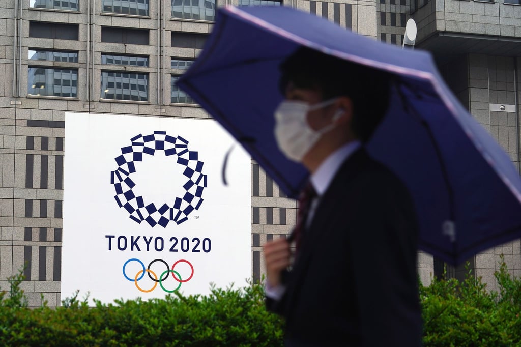 Ein Mann mit Mund-Nasen-Schutz geht im Regen an einem Banner der Olympischen Spiele Tokio 2020 vorbei.