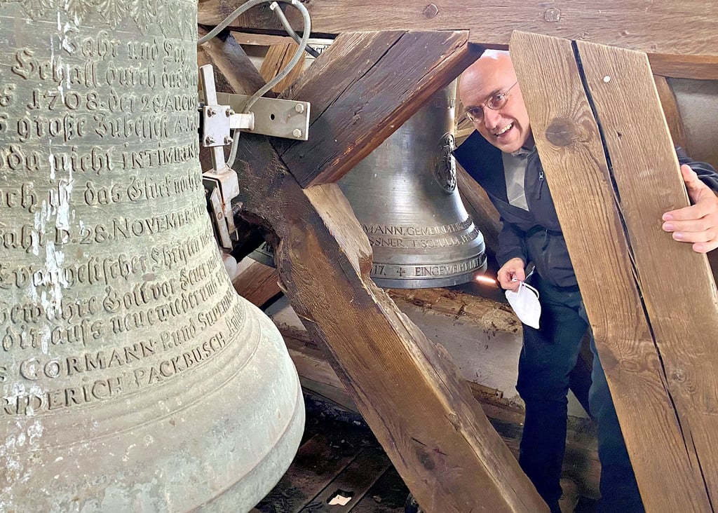 Pfarrer Thomas Meinhof vor der alten und neuen (im Hintergrund) Glocke im Turm der Seydaer Kirche. Zusammen mit den Gemeindekirchenräten hat der 54-Jährige einen neuen Service auf den Weg gebracht. Dieser verkündet um 16 Uhr hörbar eine frohe Botschaft.