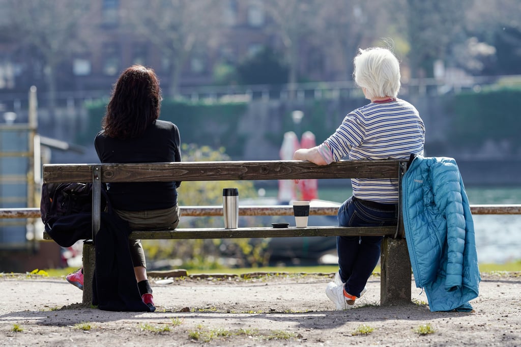 Zwei Frauen sitzen mit Abstand zueinander auf einer Parkbank