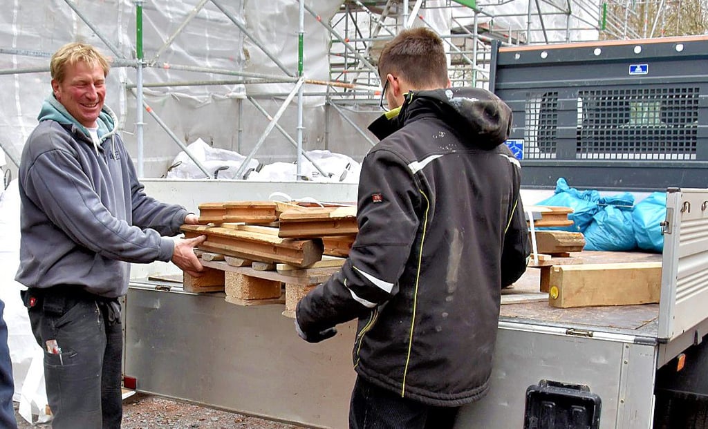 Frank Habenreich (links) und Adrian Wagner verladen Holzbohlen am neuen Standort der Stabkirche Stiege im Ortskern.