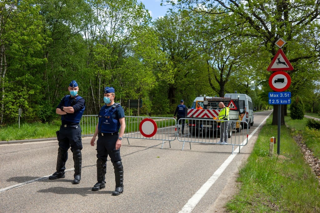 Belgische Polizisten sperren eine Straße in einem Waldstück ab.