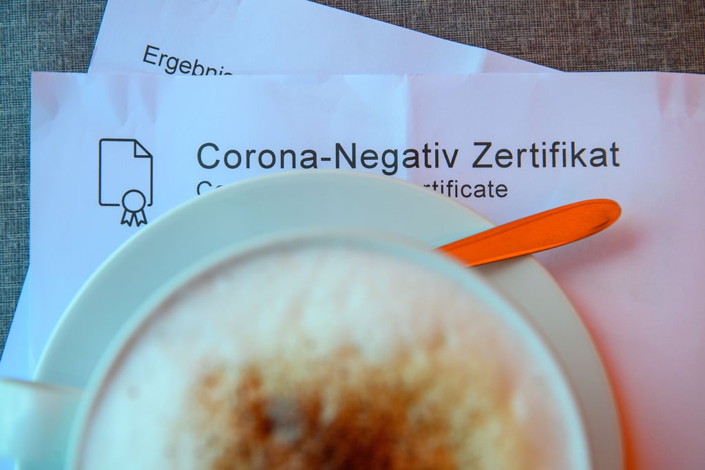 Ein Milchkaffee steht auf einem Tisch des Klosterkaffees im Kloster Unser Lieben Frauen in Magdeburg auf einem Corona-Negativ Zertifikat. Wo die Bundes-Notbremse nicht mehr gilt, darf die Außengastronomie genesene, geimpfte oder negativ getestete Gäste empfangen.