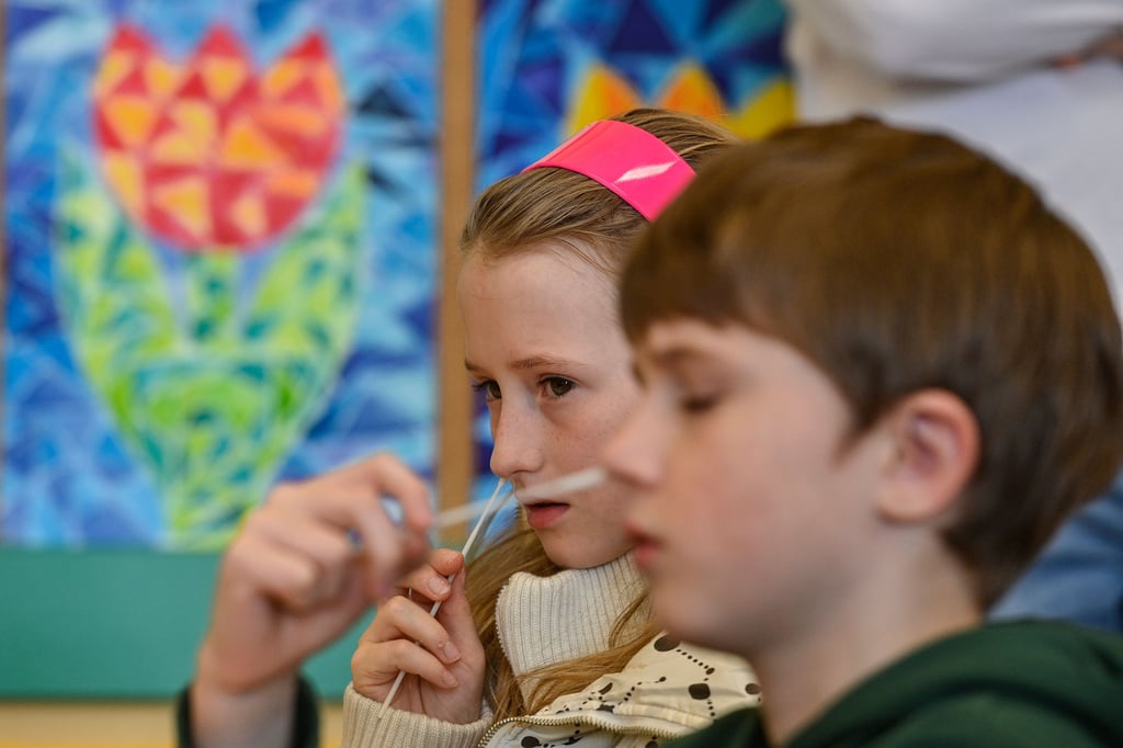 Zwei Schulkinder führen in einem Klassenraum einen Corona-Schnelltest bei sich durch