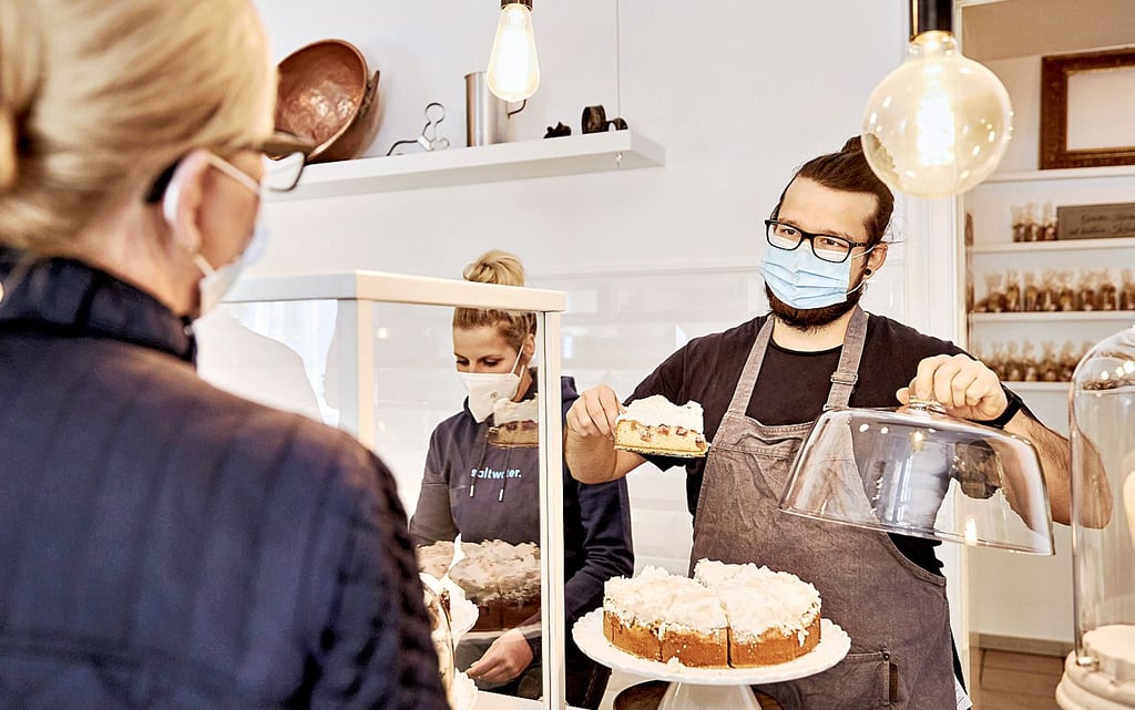 Johanna Behrends (M.) steht mit Mitarbeiter Pascal Schöpfer im Verkaufsbereich des „Verzuckert“ in Berlin. Eine Kundin ordert ein Stück Kuchen.