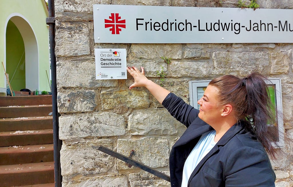 Museumsleiterin Manuela Dietz zeigt am Eingang auf die neue Plakette, die das Freyburger Jahn-Museum als Ort der Demokratiegeschichte ausweist.