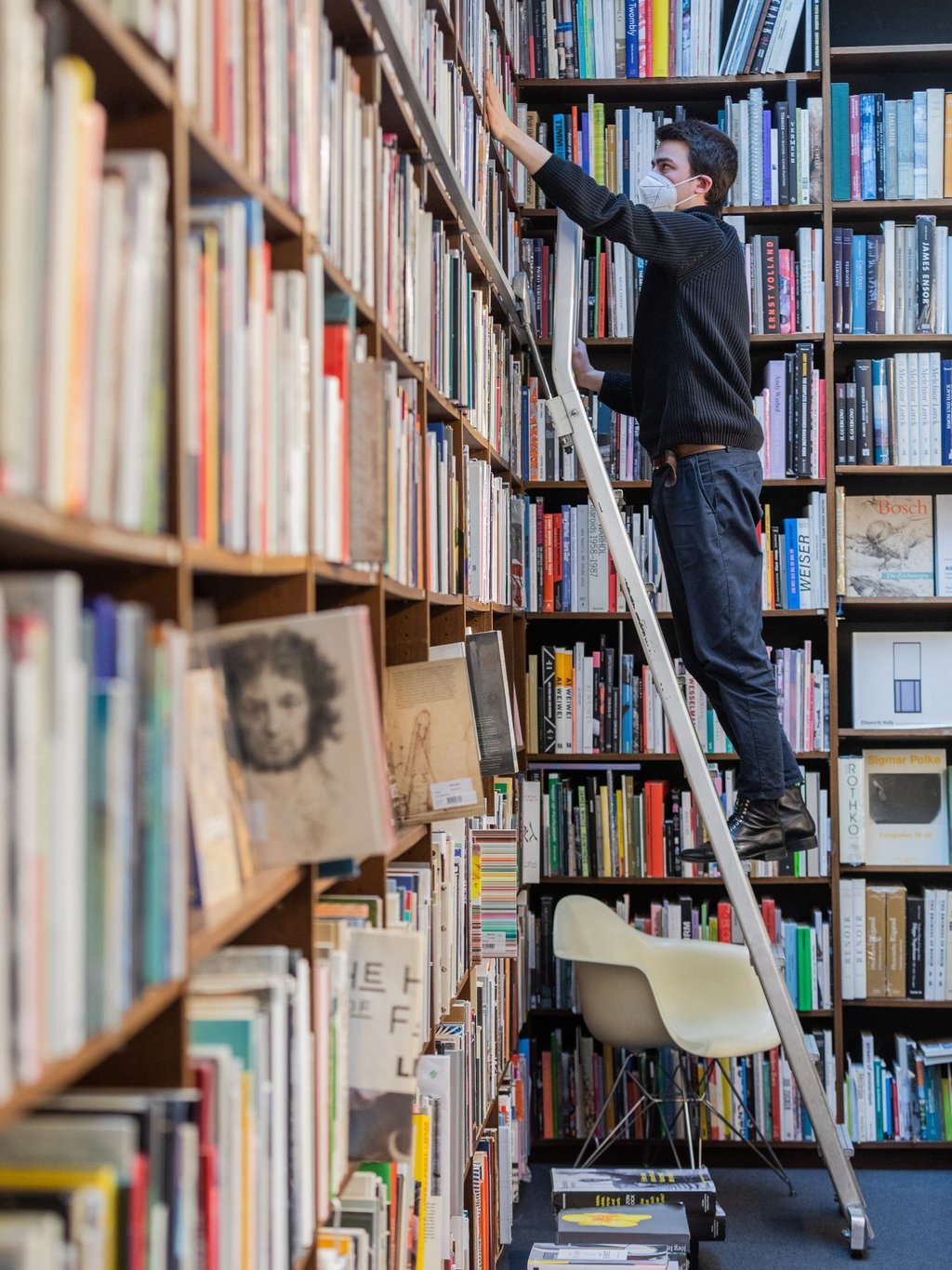 Ein Mitarbeiter steht auf einer Leiter in einer Buchhandlung.