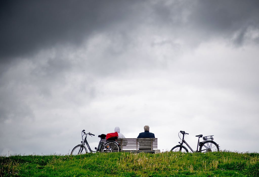 Touristen sitzen vor dunklen Wolken auf einer Bank auf dem Deich und genießen ihre Pause.