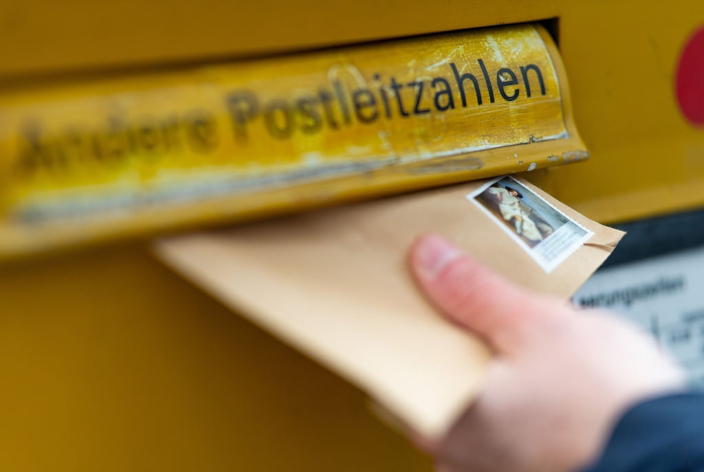 Ein Mann wirft einen Brief in einen Briefkasten.
