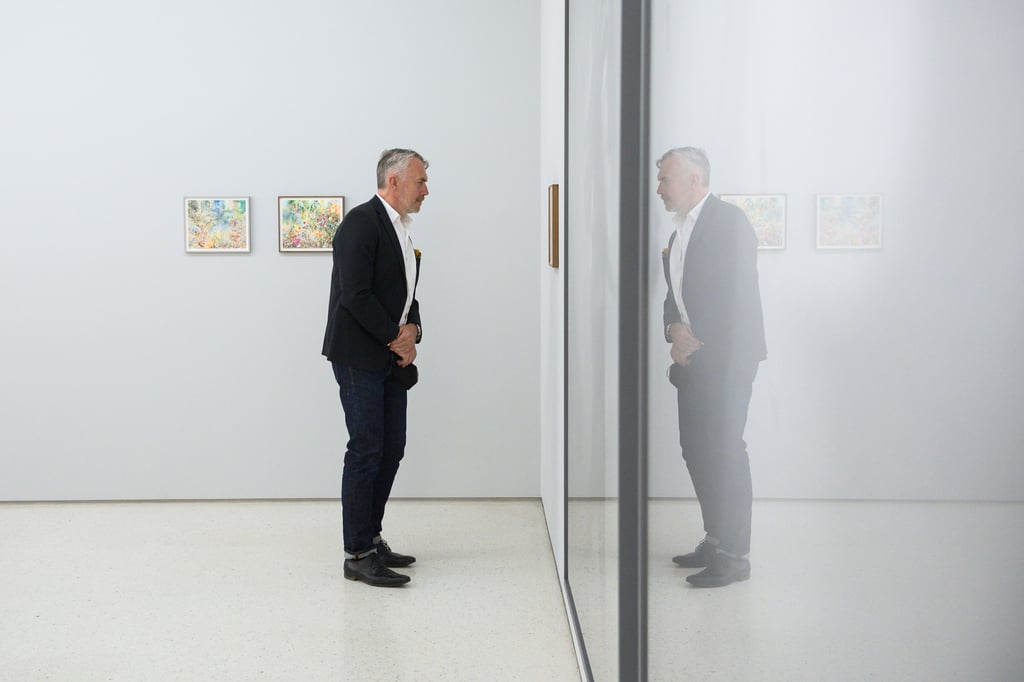 Neo Rauch sieht sich in der Grafikstiftung Neo Rauch ein Werk des Malers Stefan Guggisberg an und spiegelt sich dabei in der Scheibe des Exponats. In der Grafikstiftung eröffnete die neue Ausstellung "Vorder - Mittel - Hintergrund, Hartwig Ebersbach, Stefan Guggisberg und Neo Rauch". Die Ausstellung zeigt Werke der drei in Leipzig lebenden Künstlern Hartwig Ebersbach, Neo Rauch und Stefan Guggisberg. Die Ausstellung ist in der Grafikstiftung Neo Rauch bis zum 20.3.2022 zu sehen.