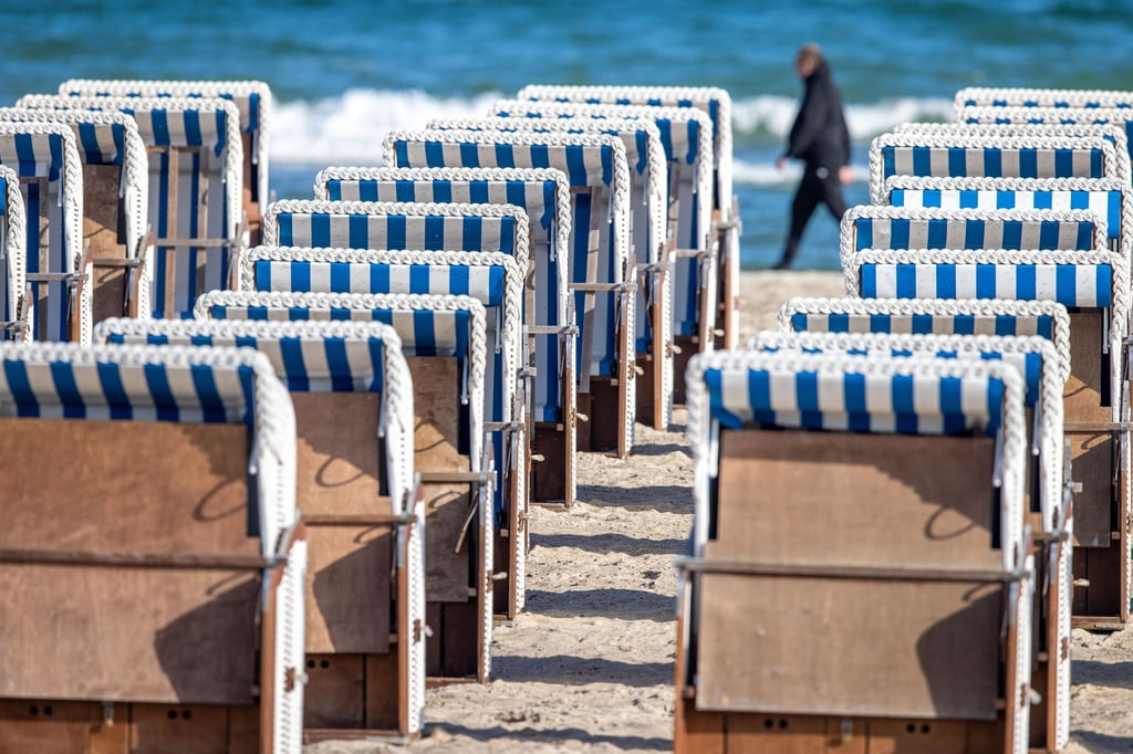 Ein Mann geht hinter leeren Strandkörben an der Ostseeküste spazieren.
