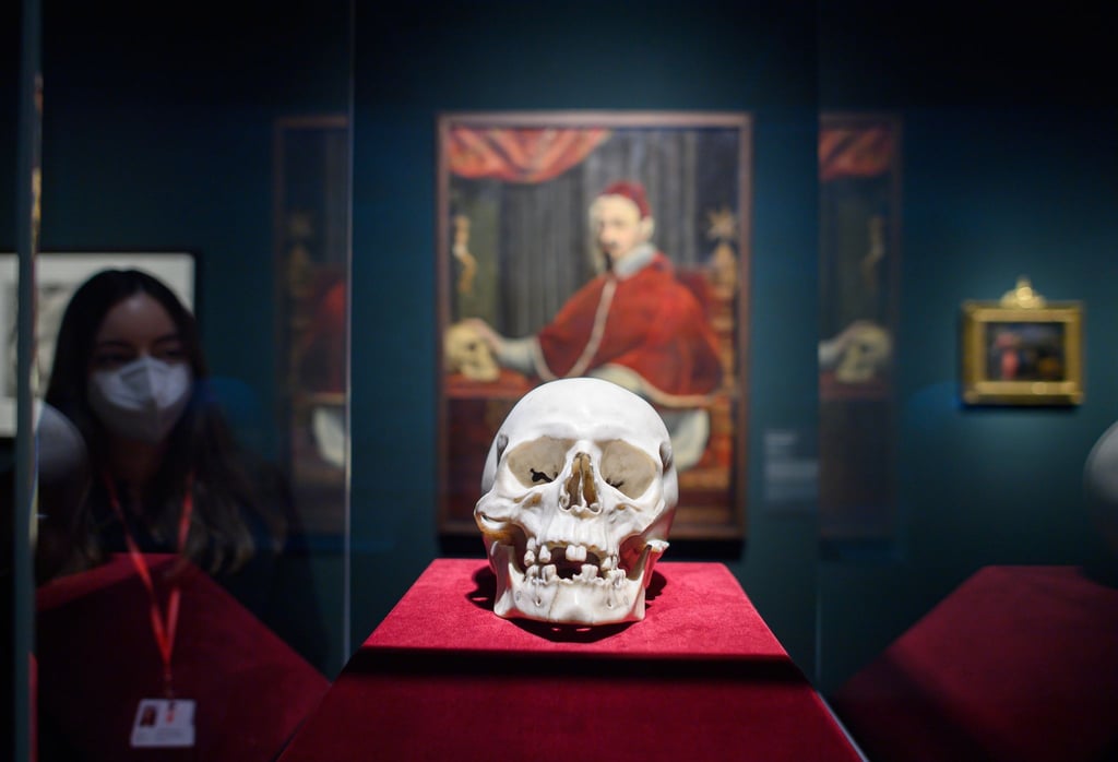 Der Totenkopf von Gian Lorenzo Bernini aus weißem Carrara-Marmor, im Hintergrund hängt das Porträt des Malers Guido Ubaldo Abbatini von Papst Alexander VII. mit Berninis Totenkopf.
