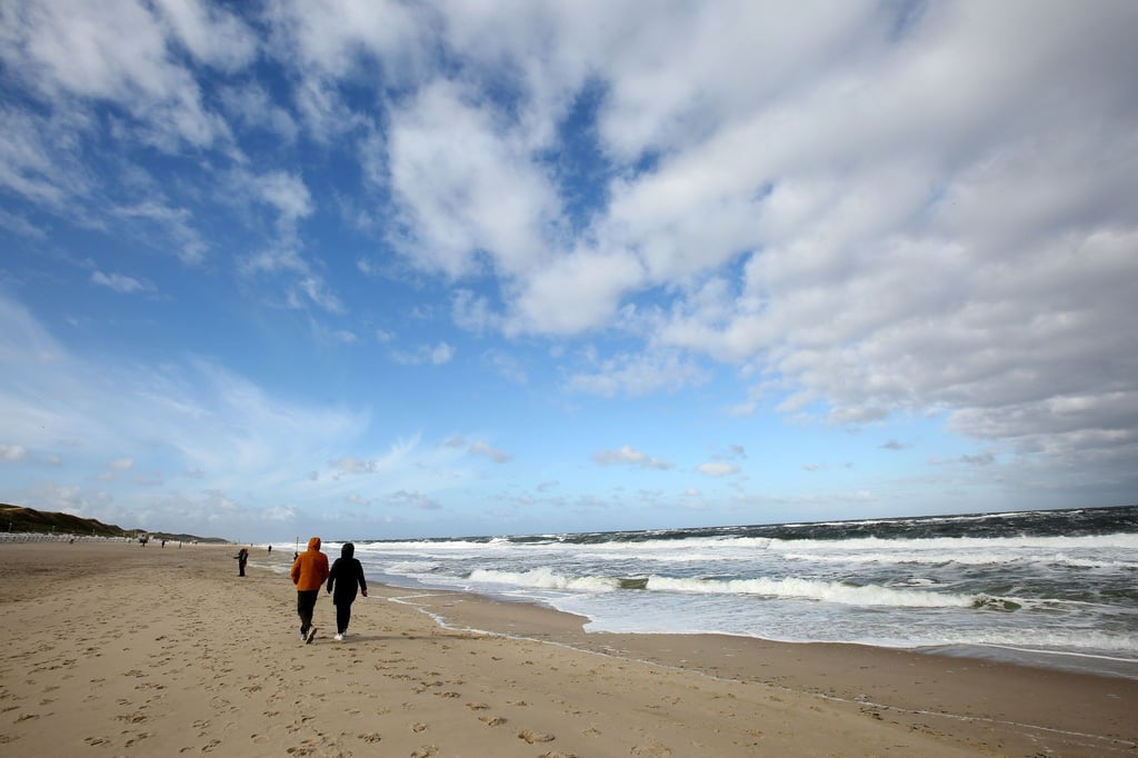 Bei windigem Wetter sind Spaziergänger am Strand unterwegs.