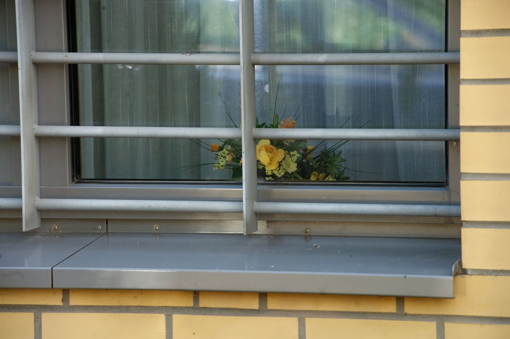 Ein Blumengesteck steht hinter einem vergitterten Fenster des Maßregelvollzugs