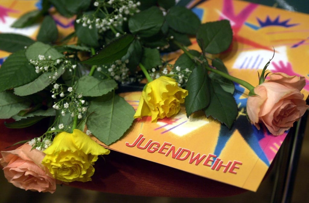 Ein Karte mit der Aufschrift Jugendweihe und Rosen liegen während einer Jugendweihefeier auf einem Tisch.