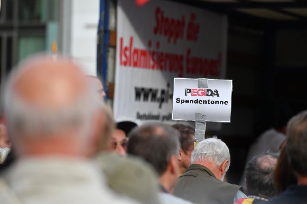 Auf einer Kundgebung von Pegida halten Anhänger ein Schild mit dem Schriftzug „Pegida Spendentonne“ in die Höhe.
