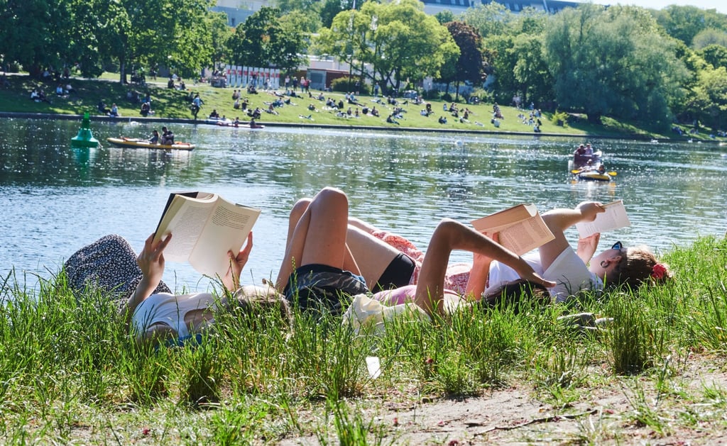 Drei Frauen liegen auf der Wiese am Landwehrkanal in Berlin und lesen Bücher.