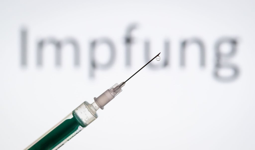 Eine Spritze wird vor den Schriftzug „Impfung“ gehalten.