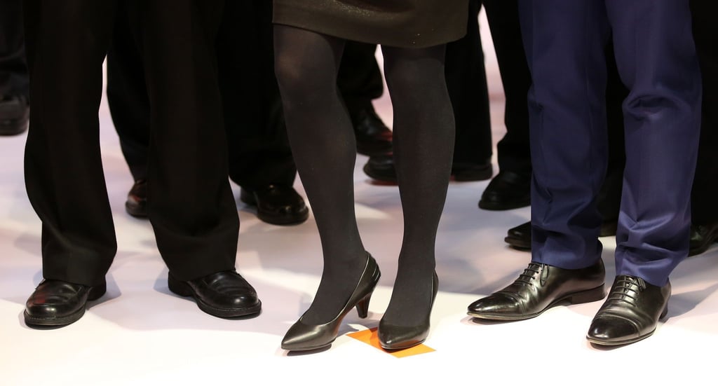 Eine Geschäftsfrau mit Pumps und Kostüm steht zwischen Geschäftsleuten mit Anzug auf einem Messestand auf der CeBIT.