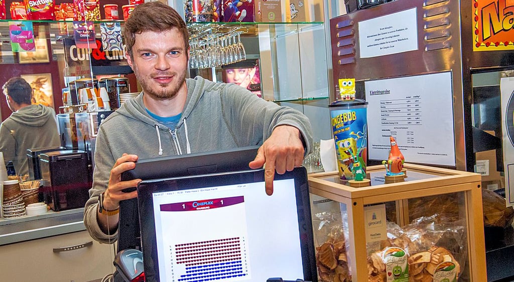 Theaterleiter Felix Seifert zeigt auf den neuen Monitor, auf dem ein Gast wie bei einer Online-Buchung die Platzbelegung eines Saales sehen kann.