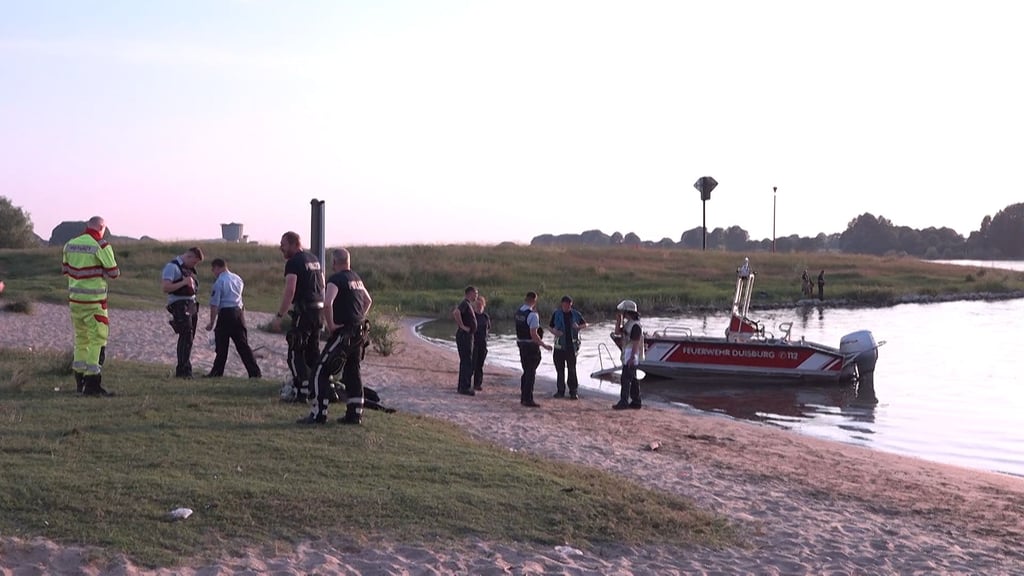 Einsatzkräfte der Polizei, Feuerwehr und DRLG arbeiten am Ufer des Rheins. Im Rhein bei Duisburg ist ein 17-jähriges Mädchen ertrunken. Nach zwei weiteren Mädchen im Alter von 13 und 14 Jahren sucht die Polizei am Donnerstagmorgen noch mit Rettungsbooten und Hubschraubern.