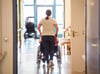 Eine Pflegerin schiebt eine ältere Frau im Rollstuhl durch einen Flur in einem Seniorenzentrum.