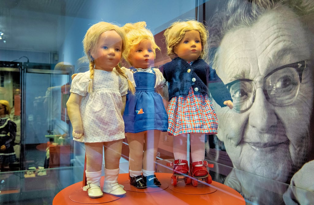 Käthe Kruse lächelt. In der Vitrine vor ihr stehen Puppen aus drei Generationen (1948, 1960, 1980). Die Ausstellung über die weltbekannte Puppengestalterin befindet sich nunmehr im Erdgeschoss der Kunsthalle des Romanischen Hauses in Bad Kösen.