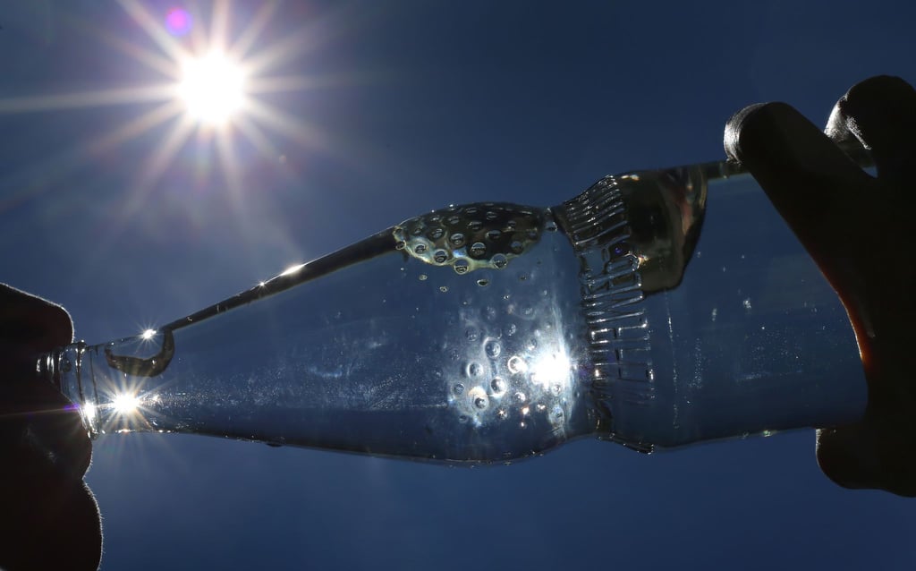 Eine Frau trinkt im Sonnenschein aus einer Flasche sprudelndes Mineralwasser.